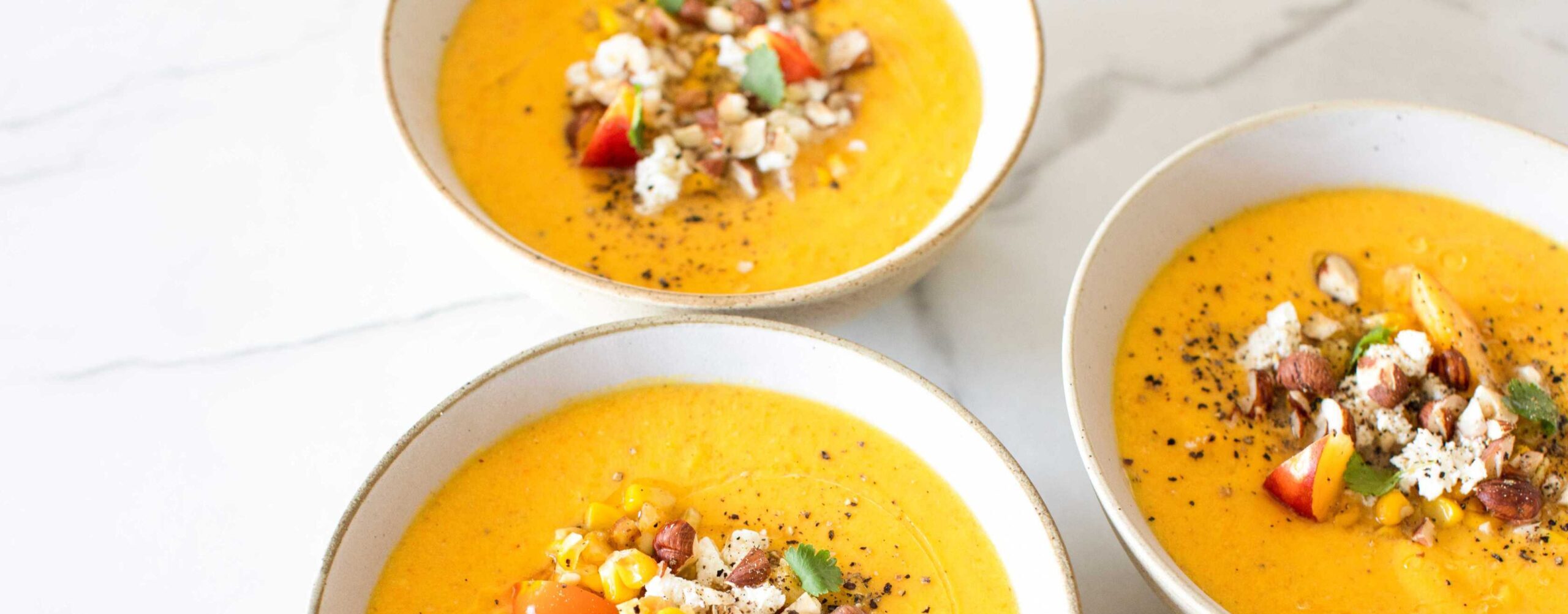 Three bowls of orange soup with colorful accompanments in middle of bowl